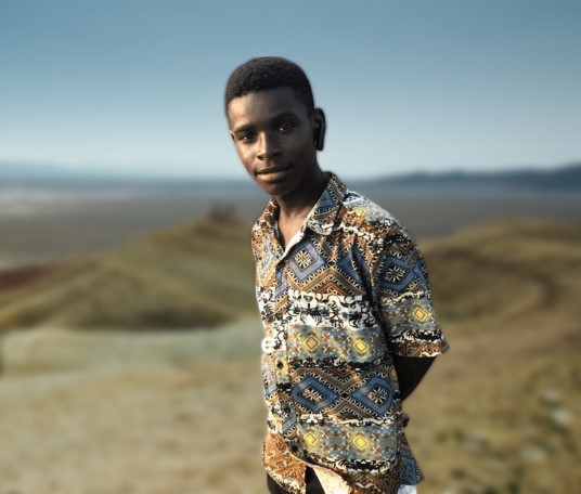 Jomasco Waves outdoors in a patterned shirt, Nzema backdrop